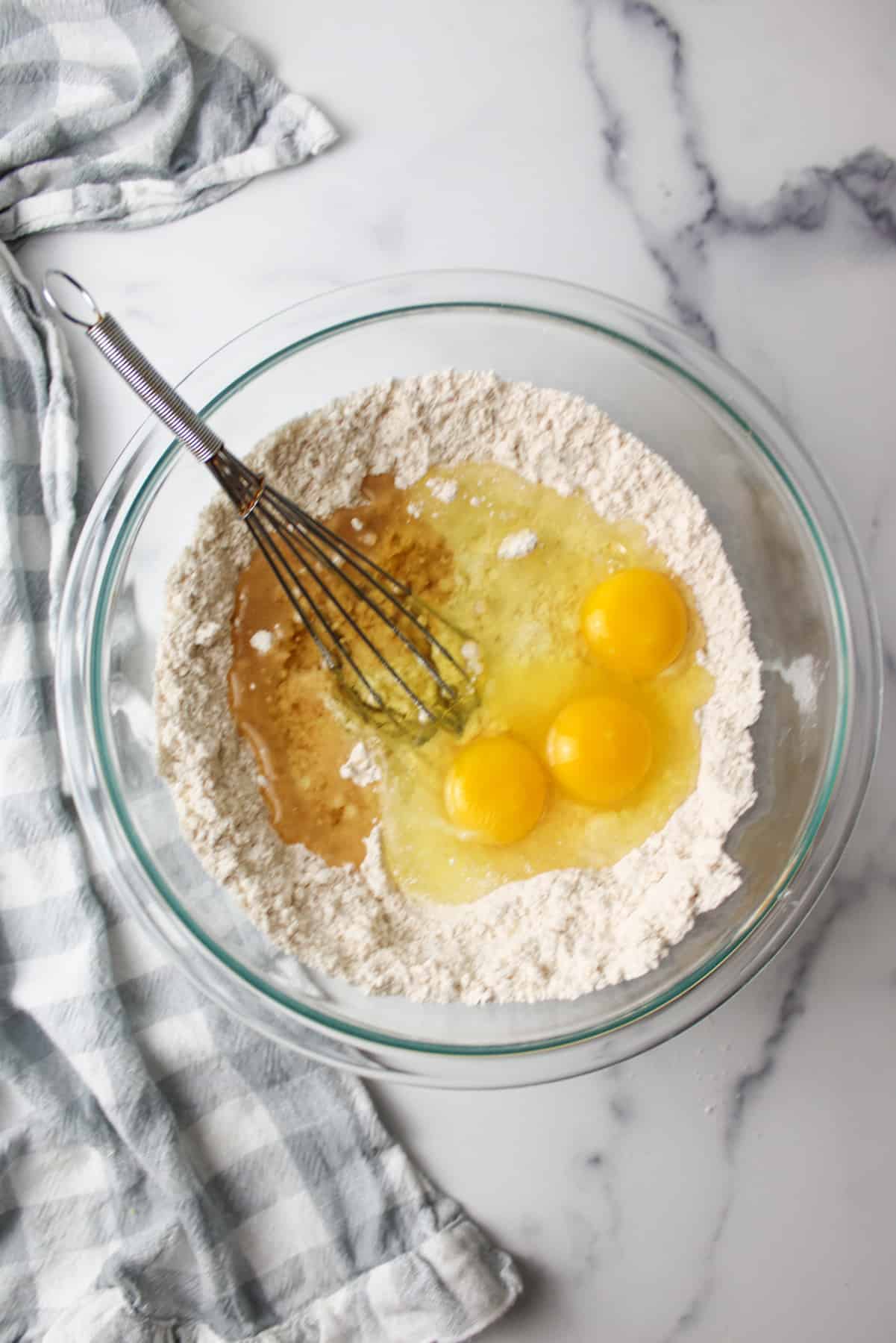 eggs and oil added to dry ingredients in a mixing bowl with a whisk
