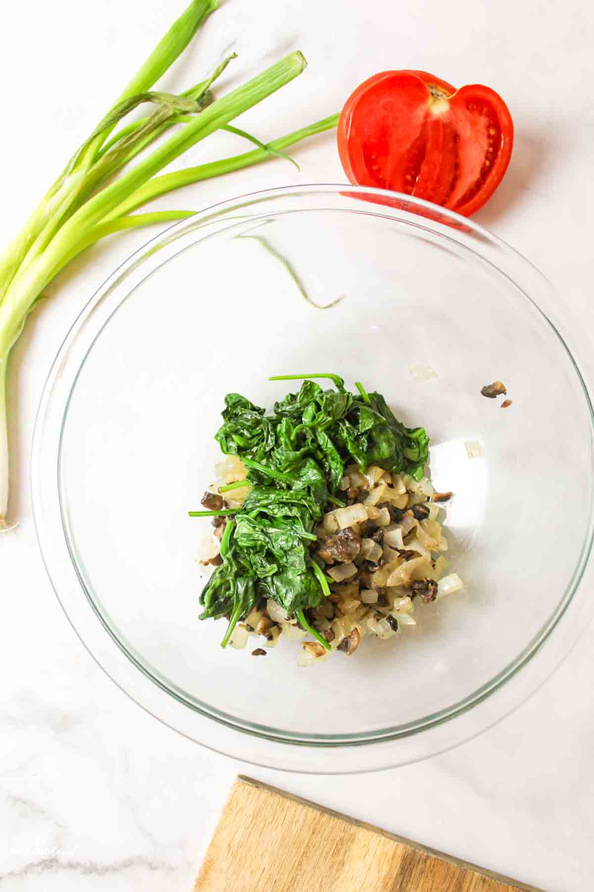 Cooked spinach, mushrooms, onions in glass mixing bowl.