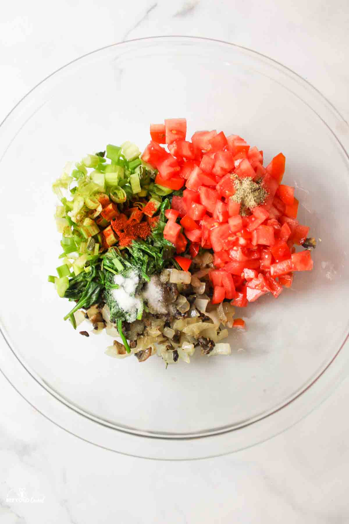 Tomatoes, green onions, seasonings, cooked mushrooms, spinach, onions in glass bowl.