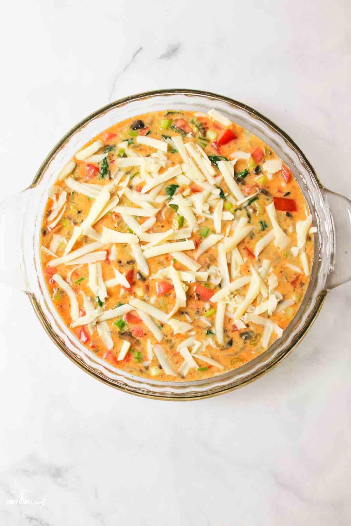 cheese topped raw veggie quiche in a pie plate