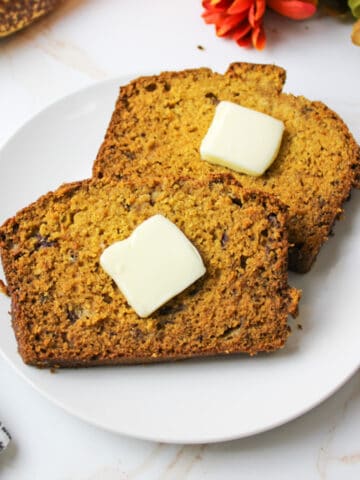 two slices of pumpkin banana bread on a plate topped with butter pads