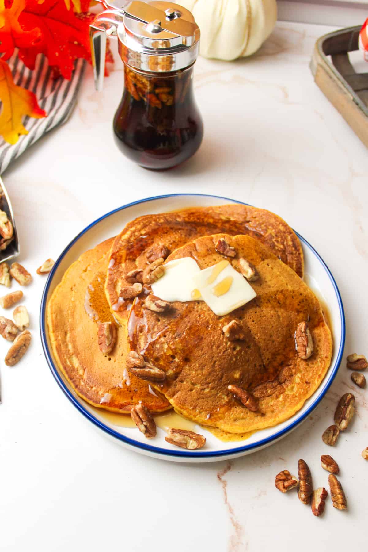 a plate filled with pumpkin pancakes and topped with pecans and syrup and butter