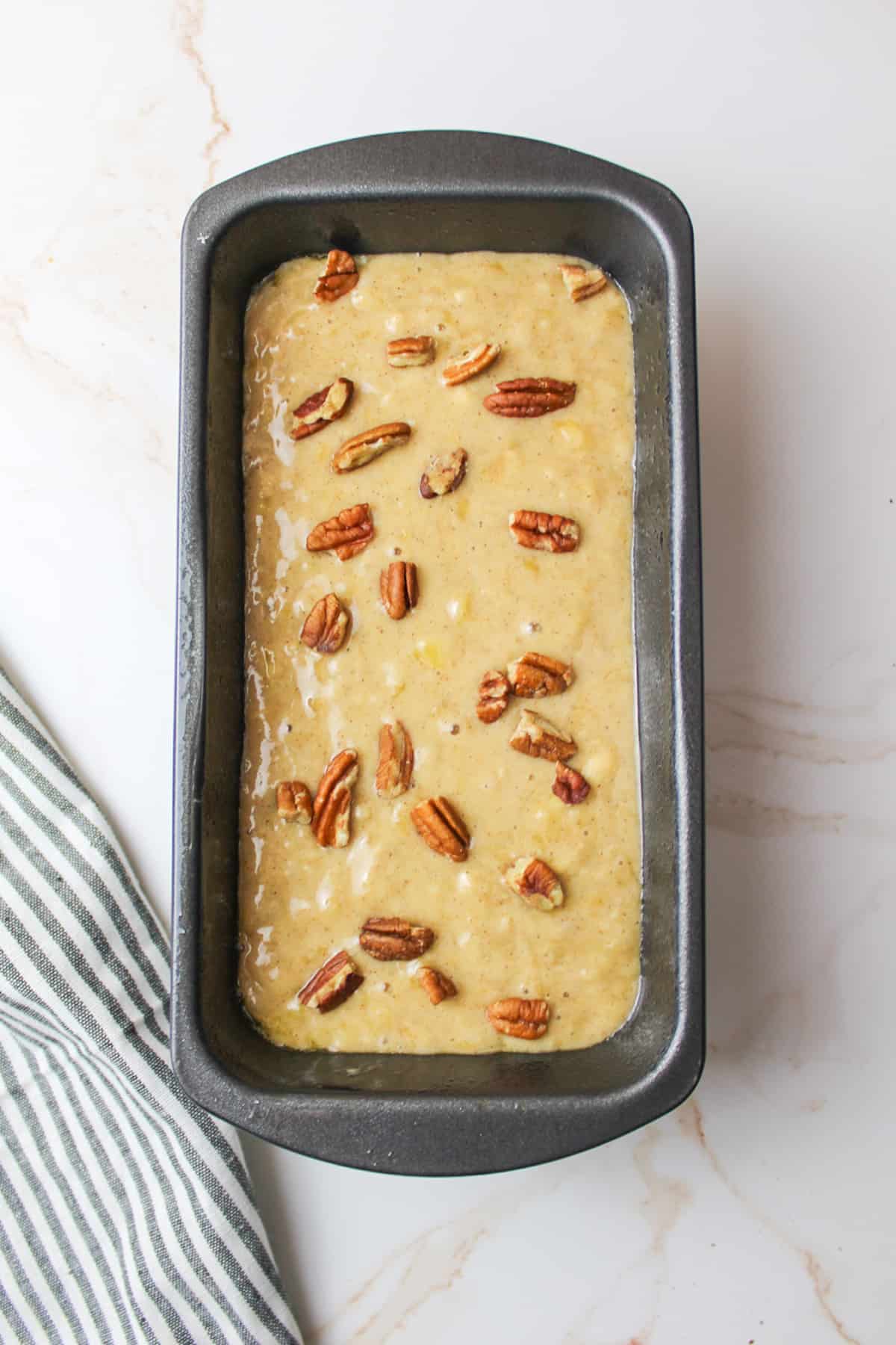 pecans on top of pumpkin spice banana bread batter in a bread loaf pan
