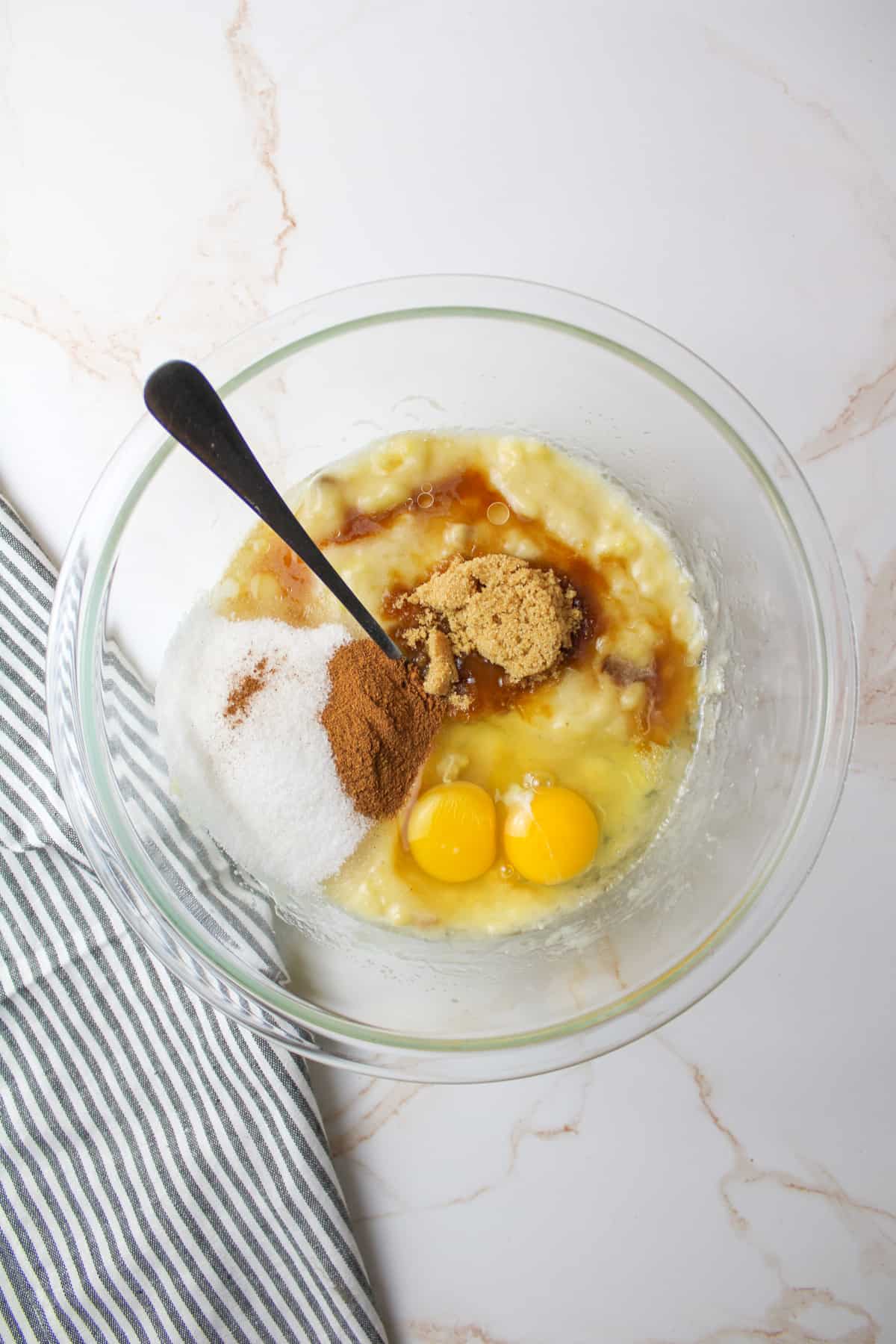 mashed banana with sugars and eggs and oil in a bowl with a fork