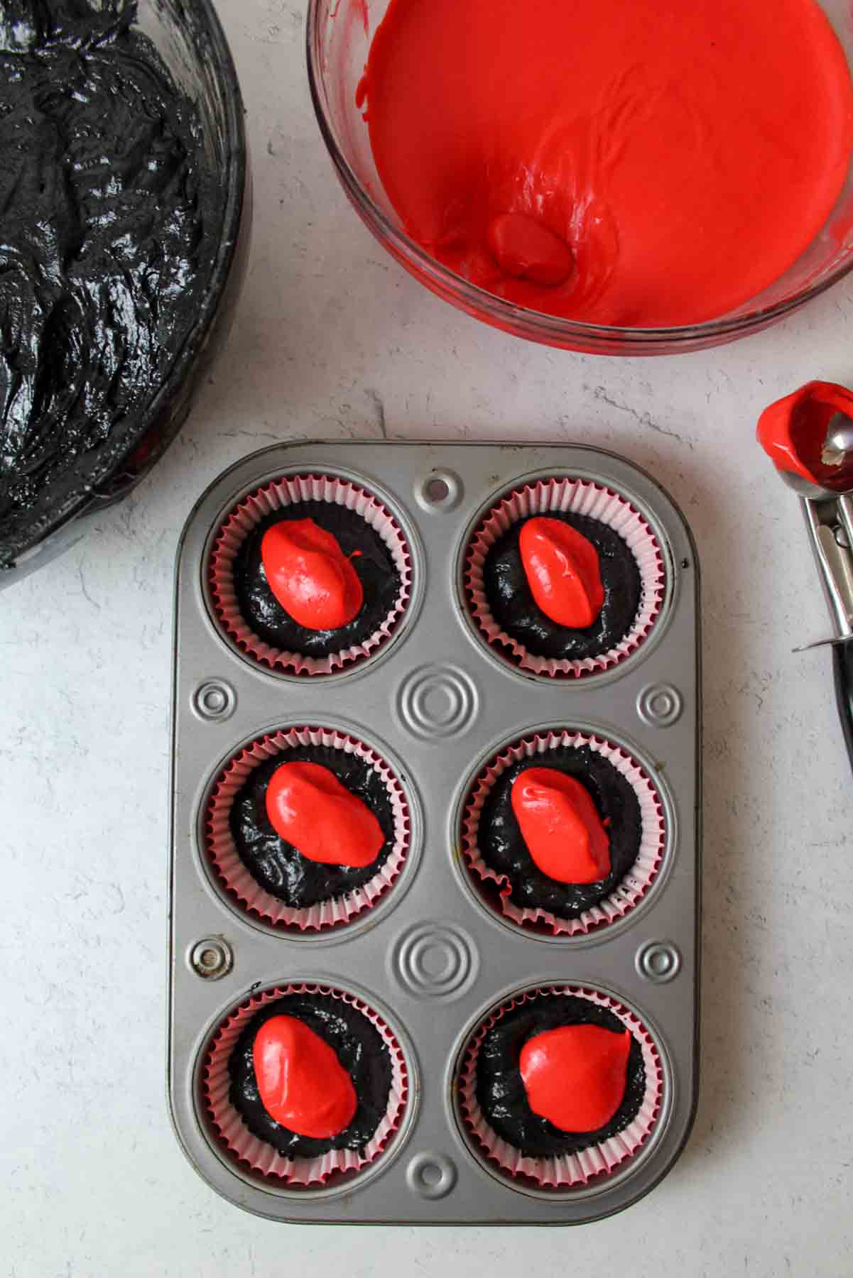 red filling dolloped on top of black cupcake batter in lined muffin tin