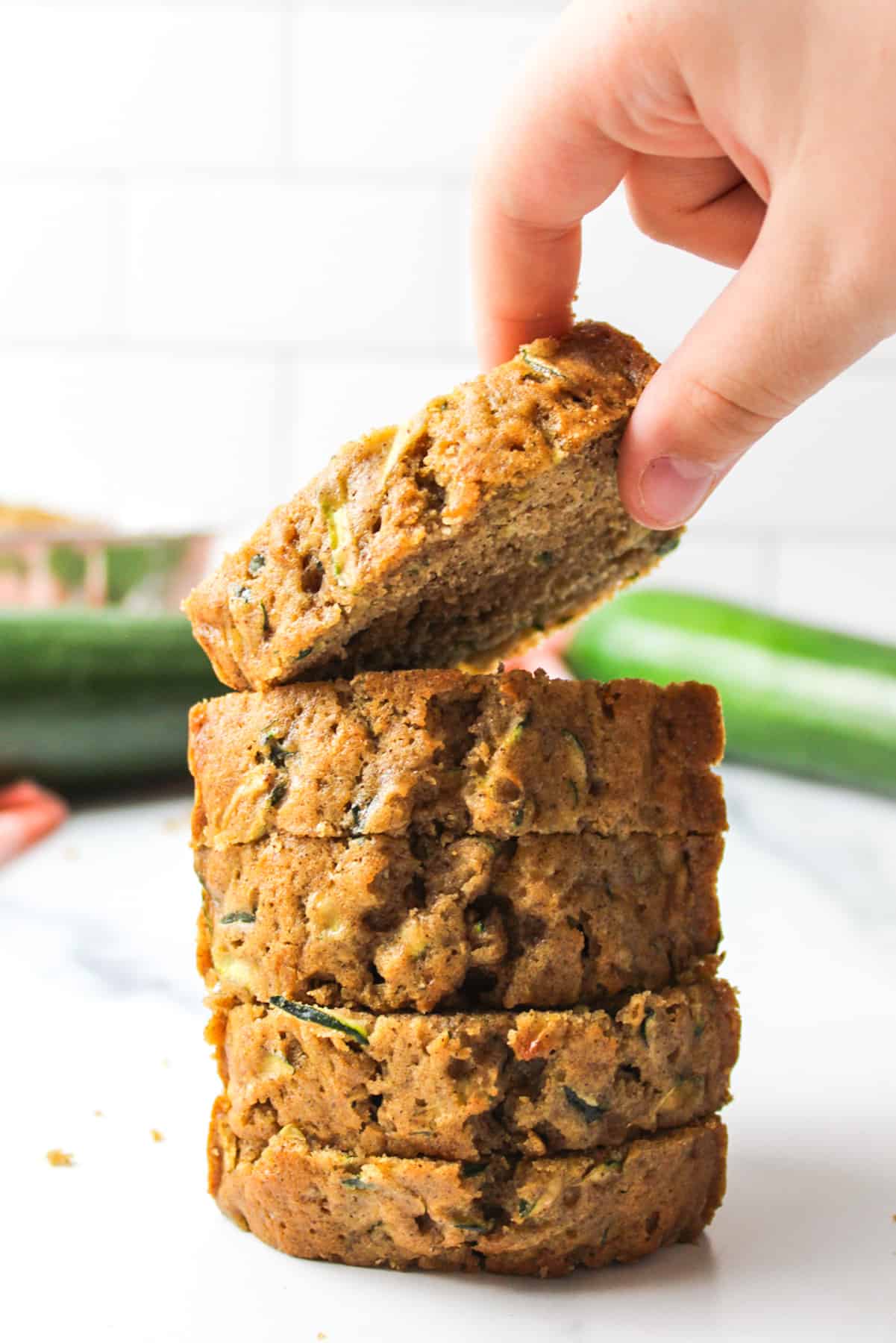 a hand picking up a slice of zucchini bread from a stack of slices