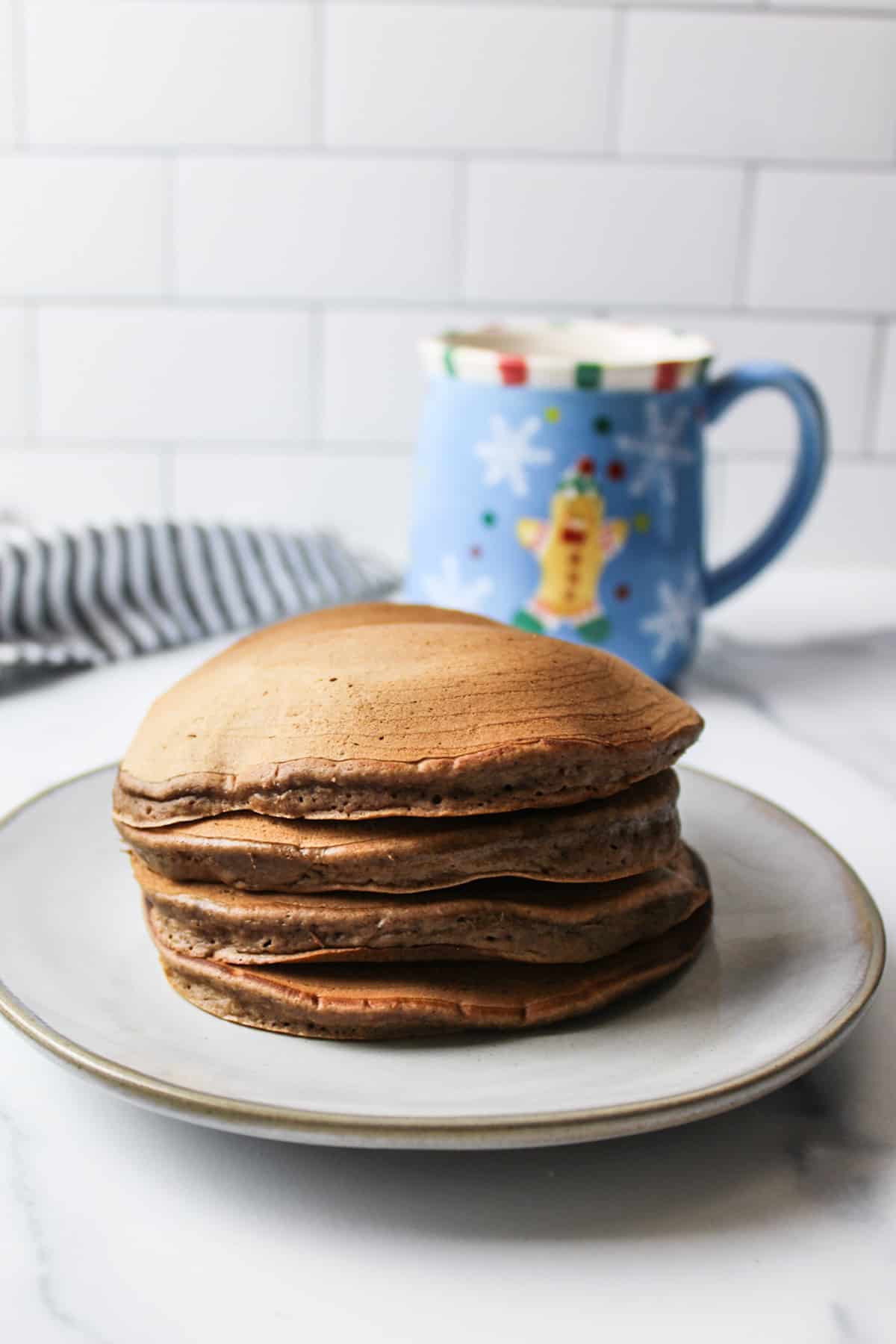 stack of hot chocolate pancakes on a plate with blue mug in background