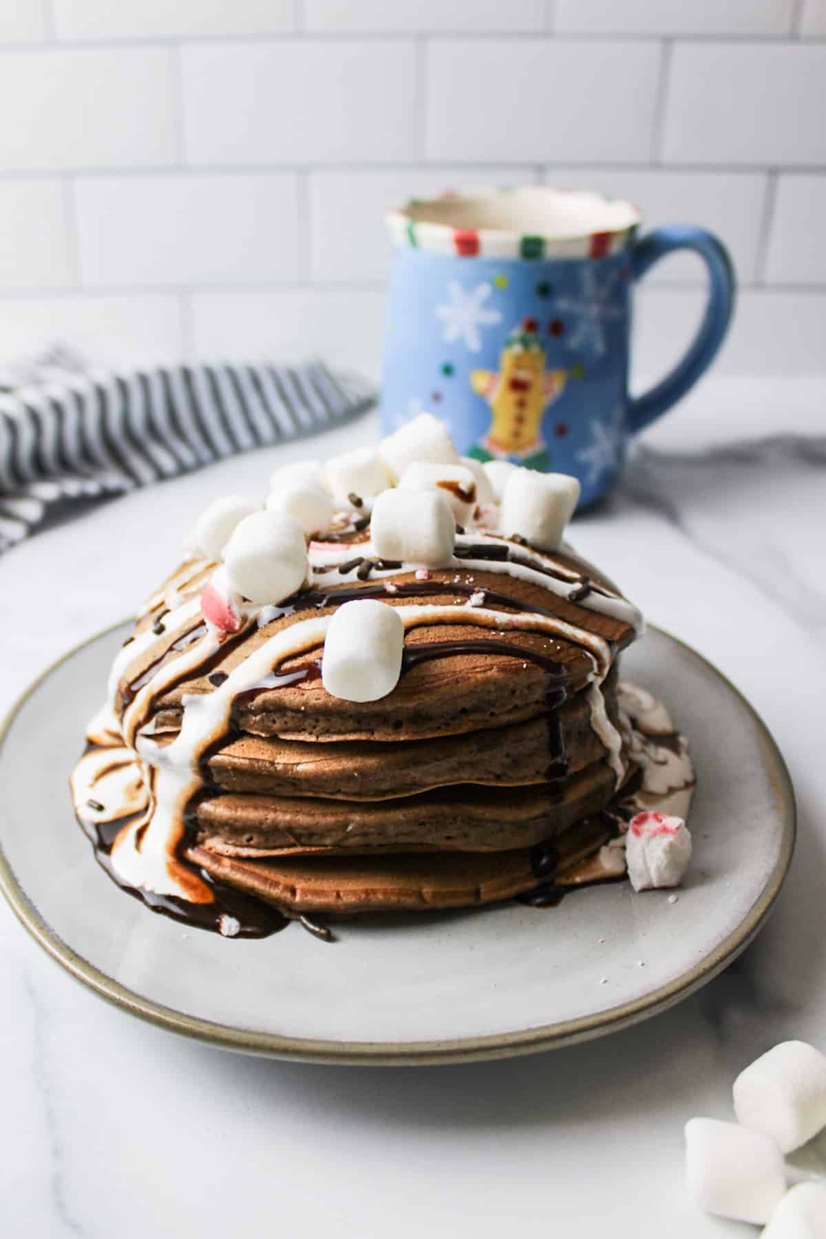 stack of hot chocolate pancakes on a plate topped with chocolate syrup and marshmallows.