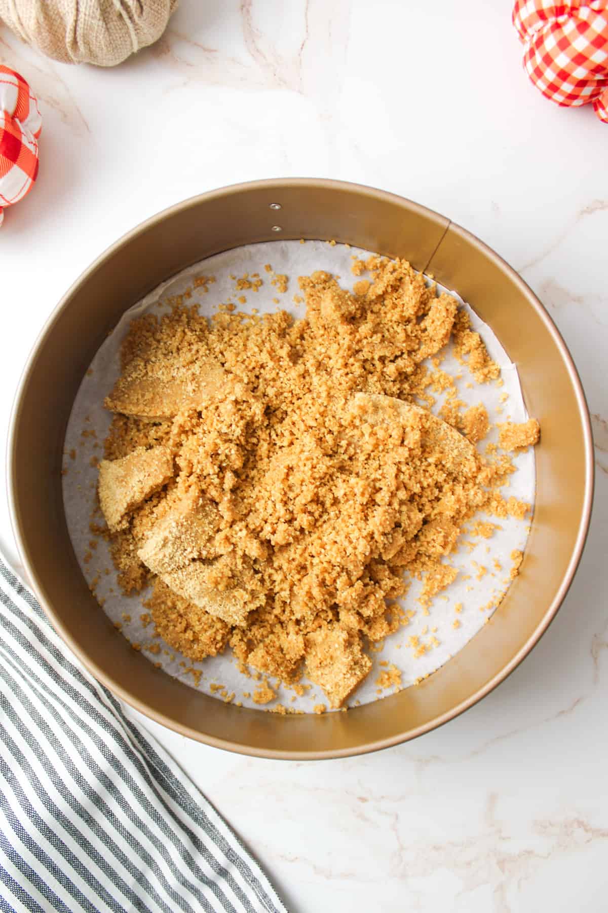 graham cracker crust mixture piled into a springform pan lined in parchment paper