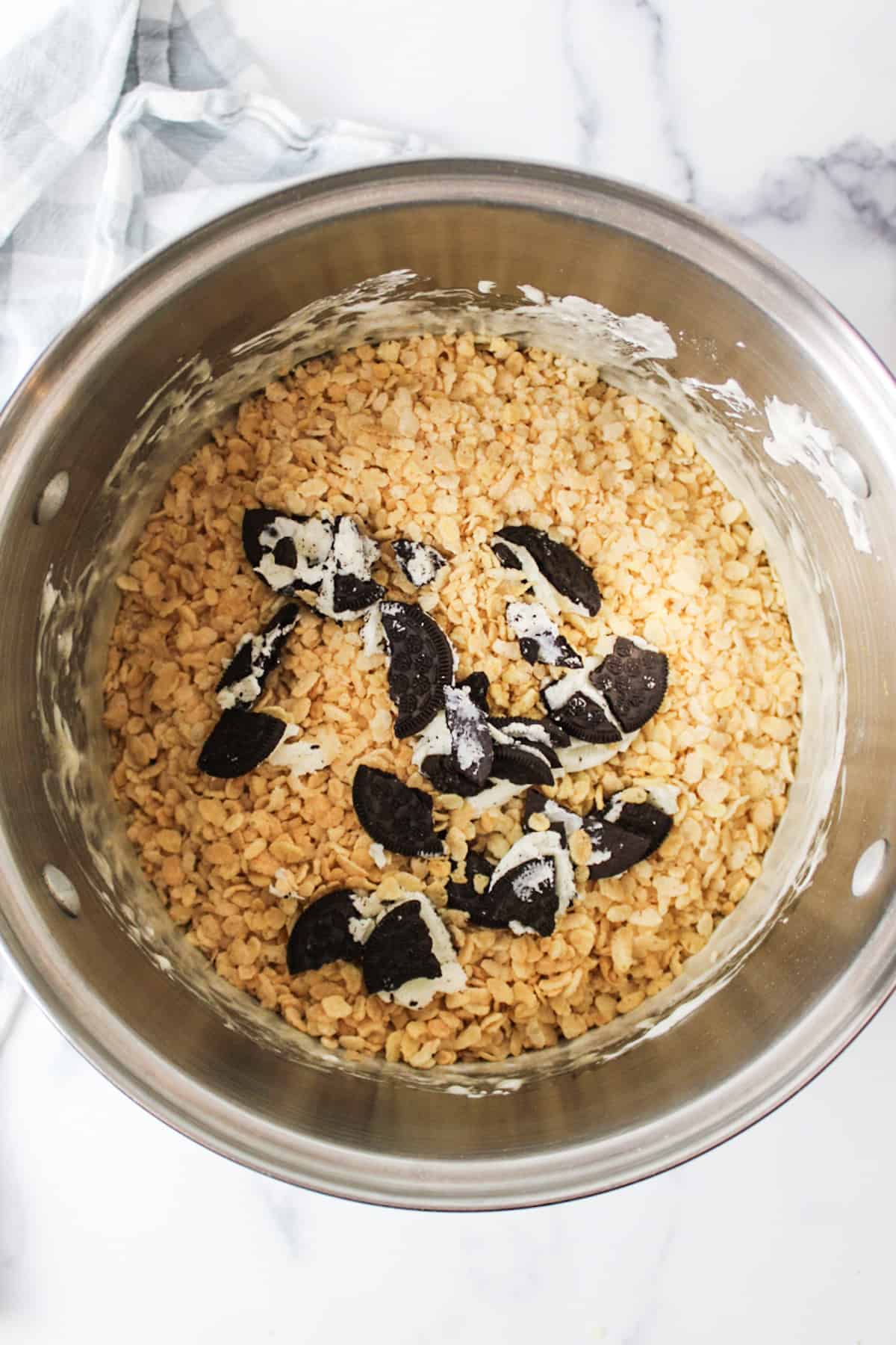 rice krispy cereal and broken oreos added to a pot of melted marshmallows.