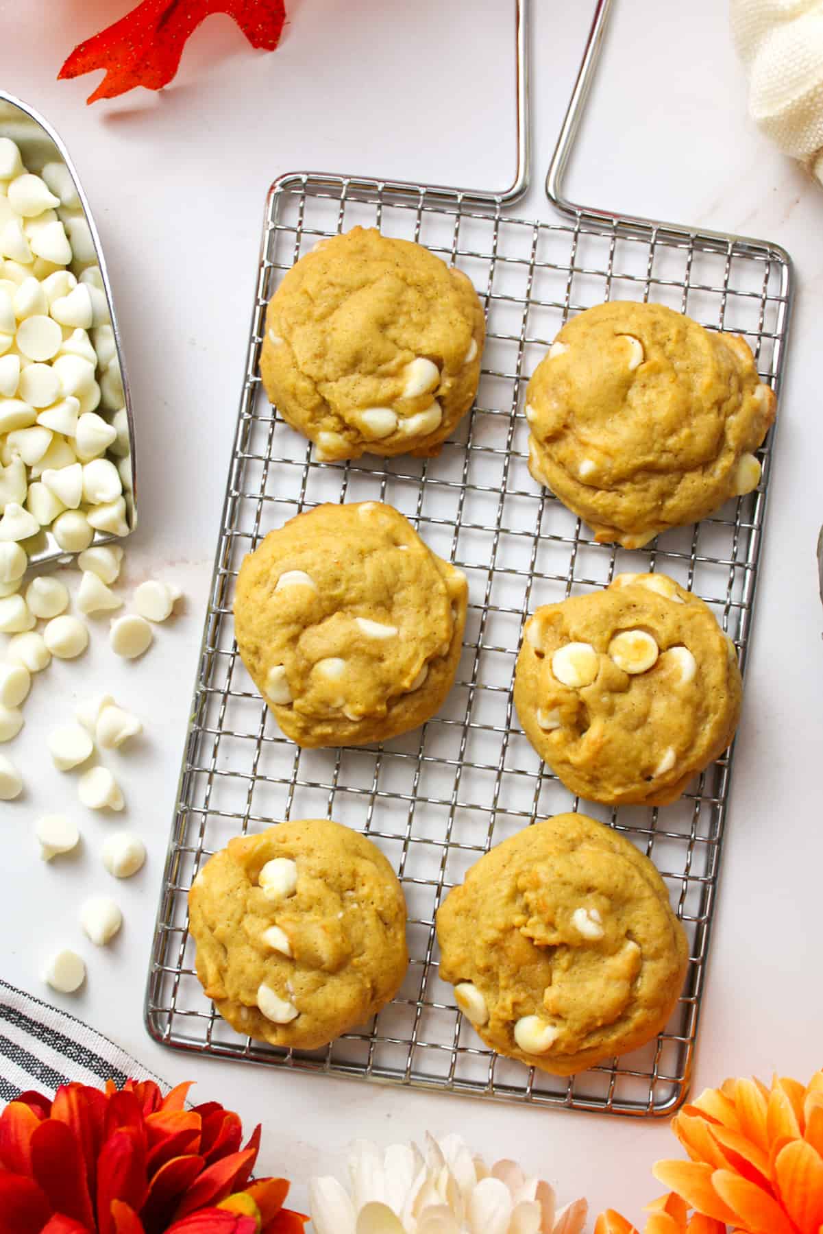 6 pumpkin white chocolate chip cookies on a wire rack with white chocolate chips to the side.