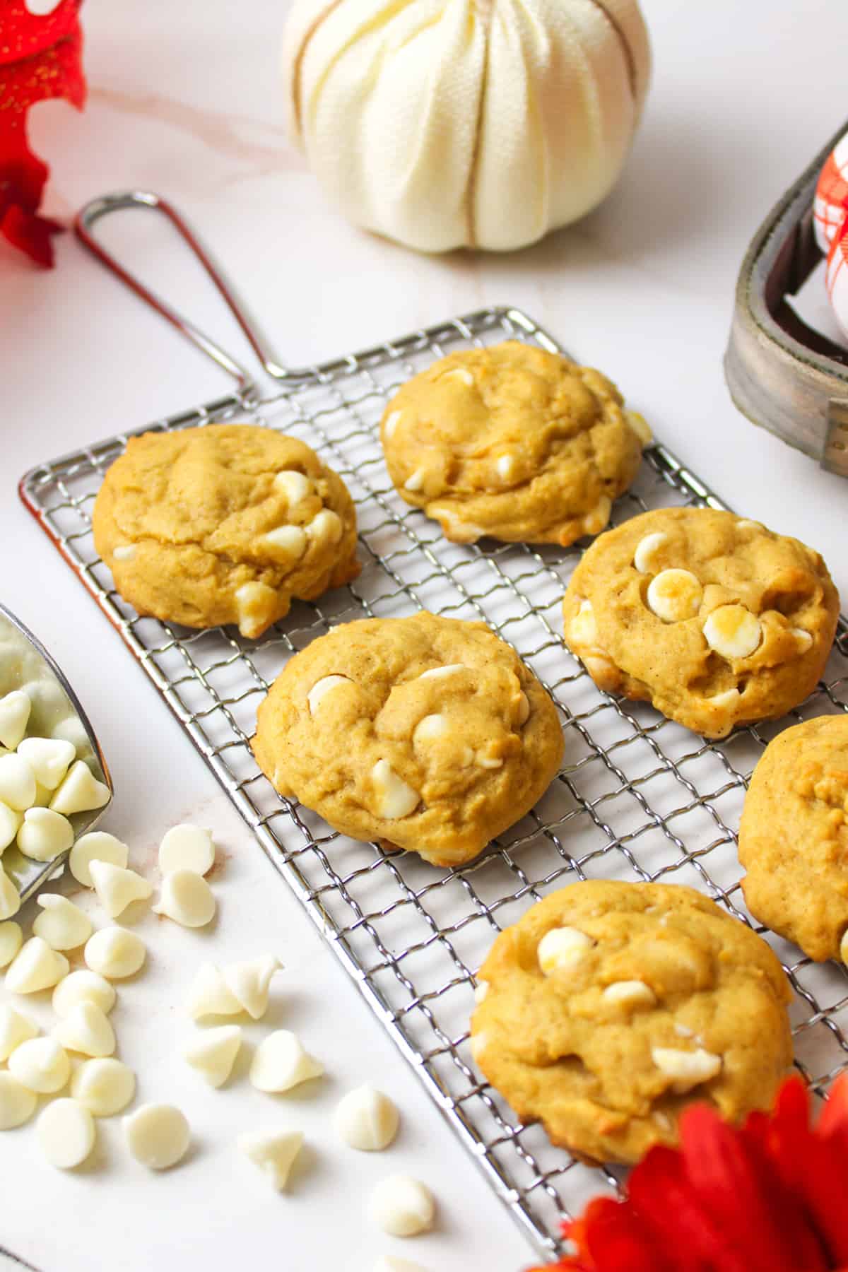 6 pumpkin white chocolate chip cookies on a wire rack with white chocolate chips.