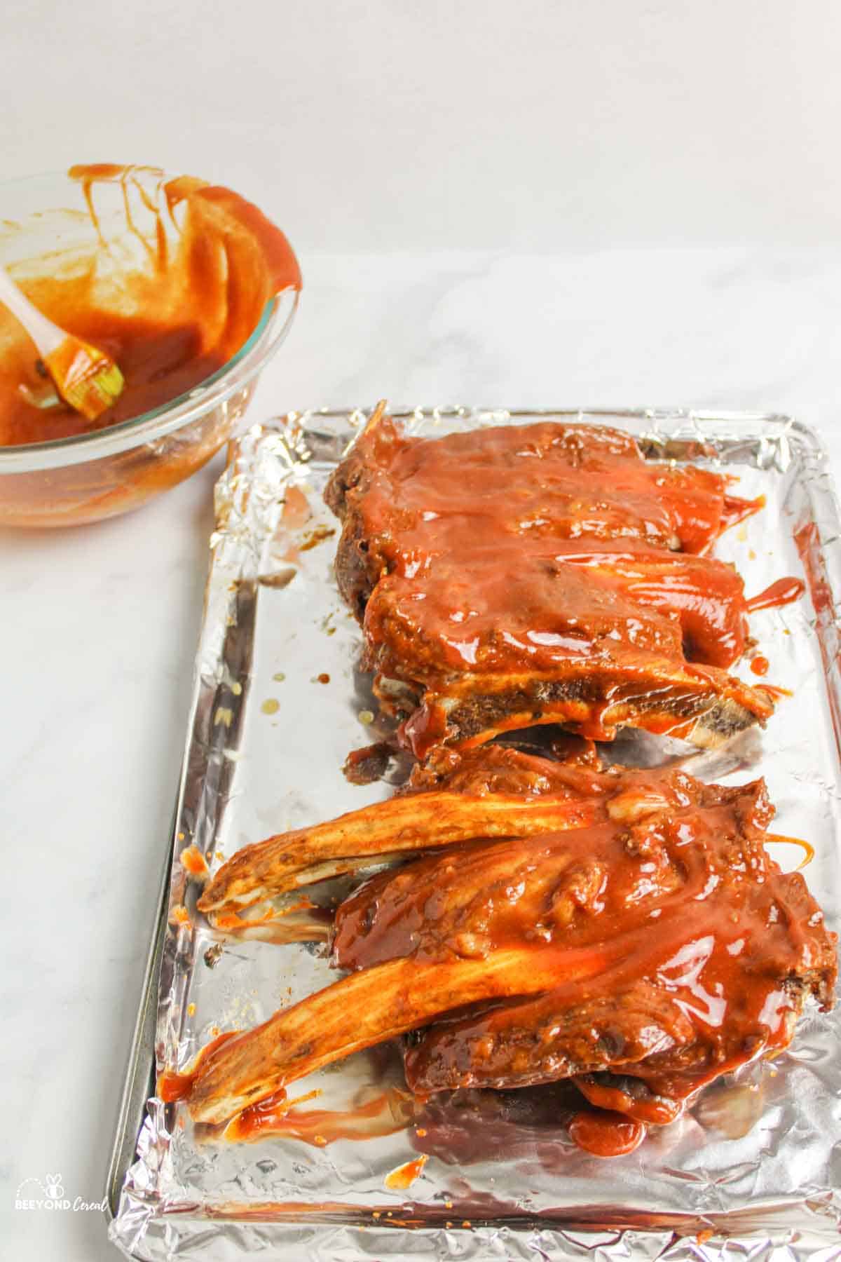 bbq sauce covered beef ribs on foil lined baking sheet