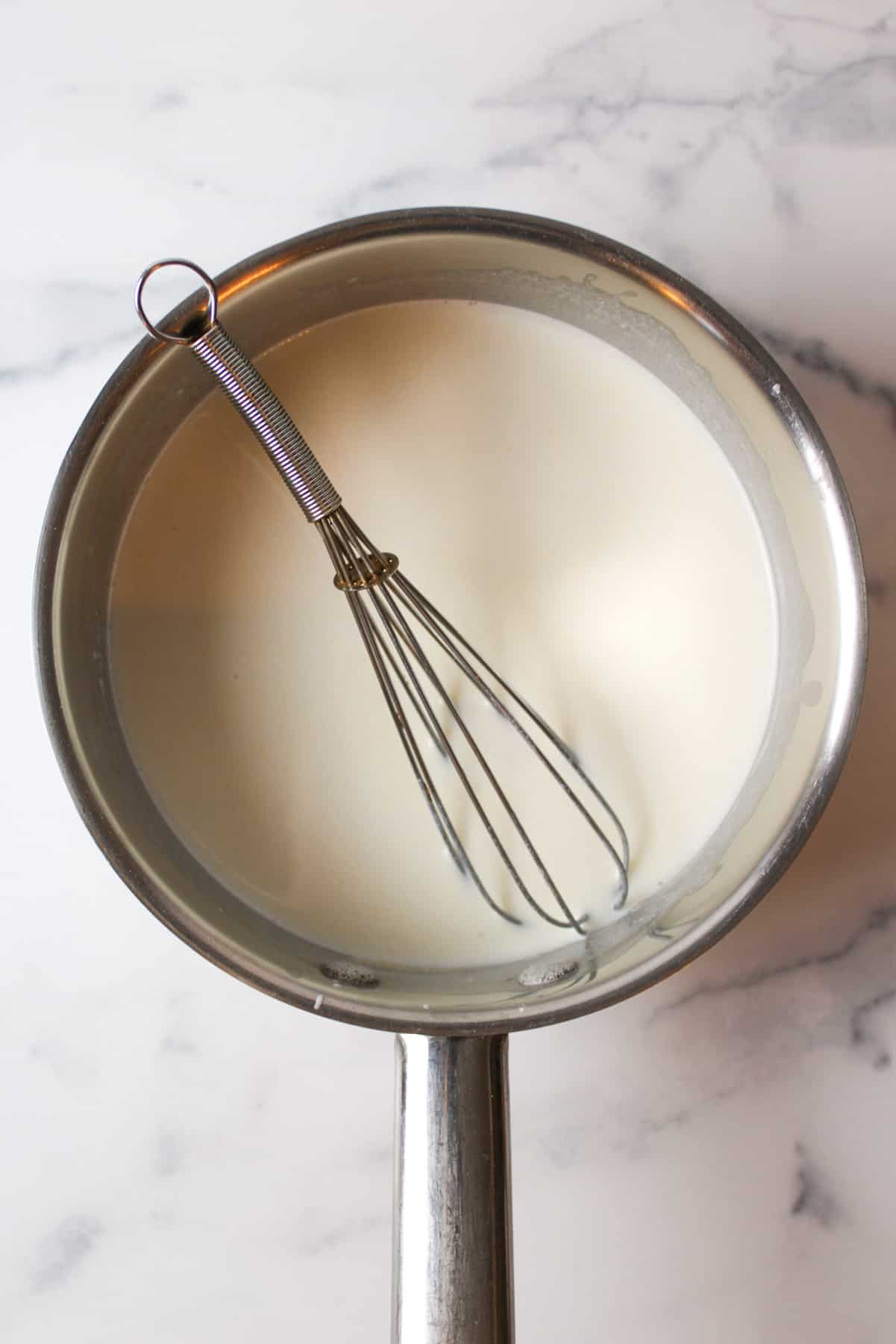 roux sauce in a medium sized pot with a metal whisk.
