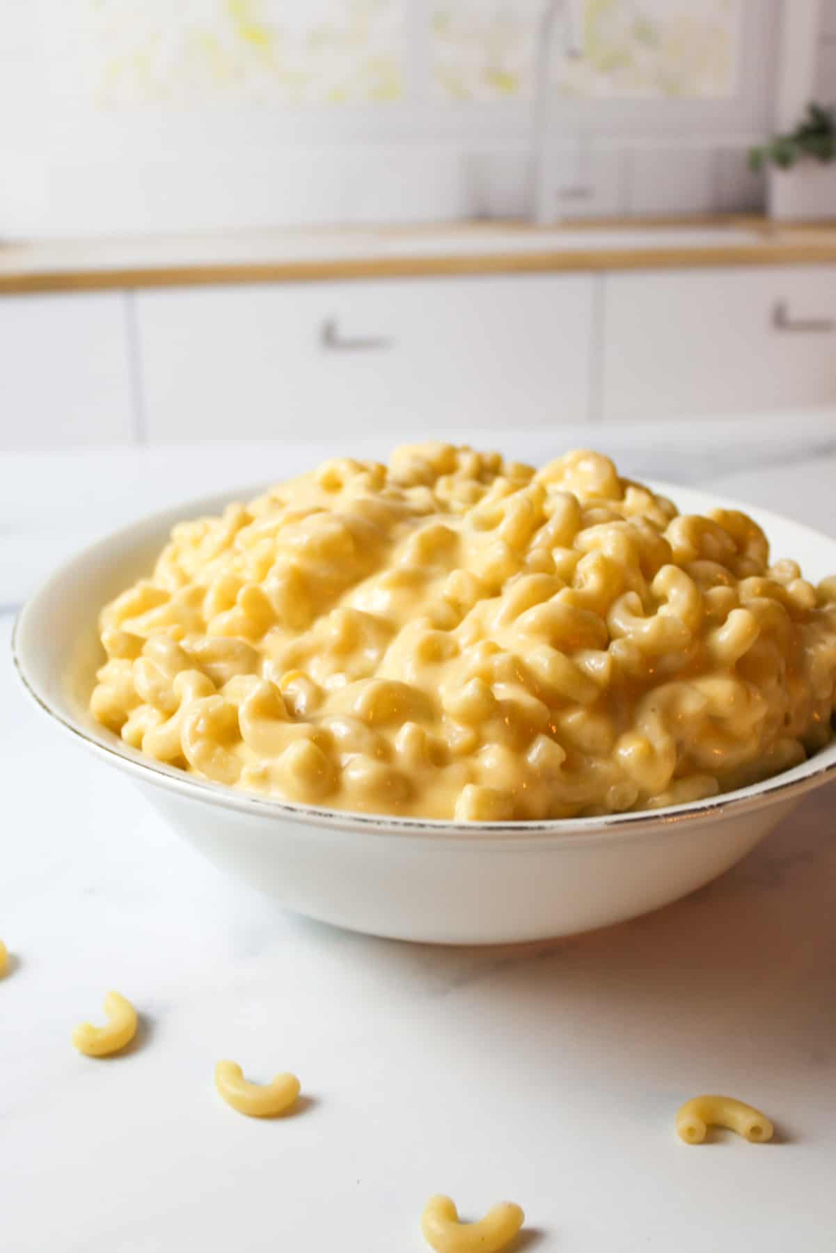 a creamy bowl filled with mac and cheese with some scattered elbow noodles around it.