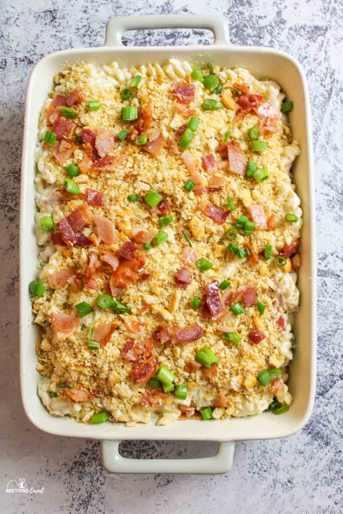 Bacon Cream Cheese Pasta in a baking dish topped with ritz cracker crumbs green onions and bacon pieces