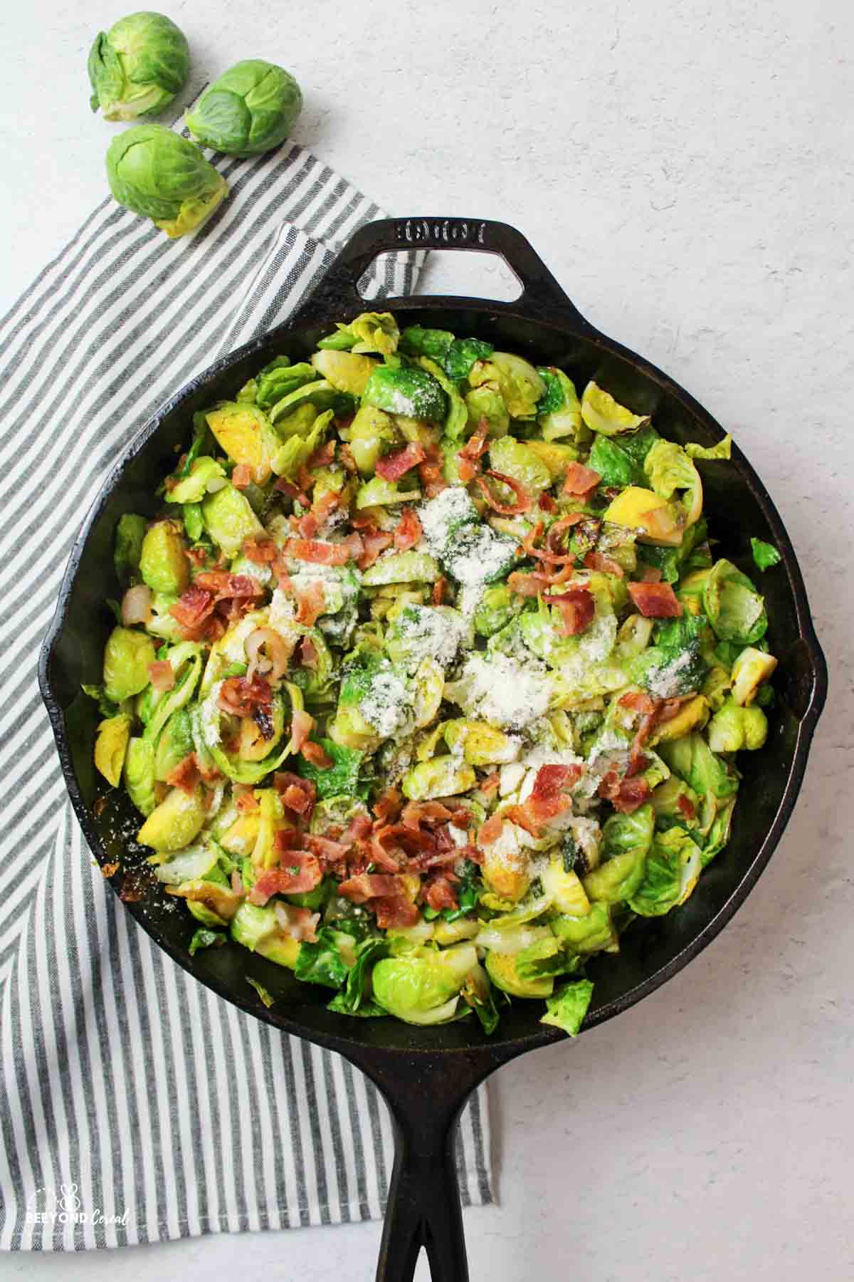 brussel sprouts in a cast iron skillet with chopped bacon and dry ranch seasoning on top.
