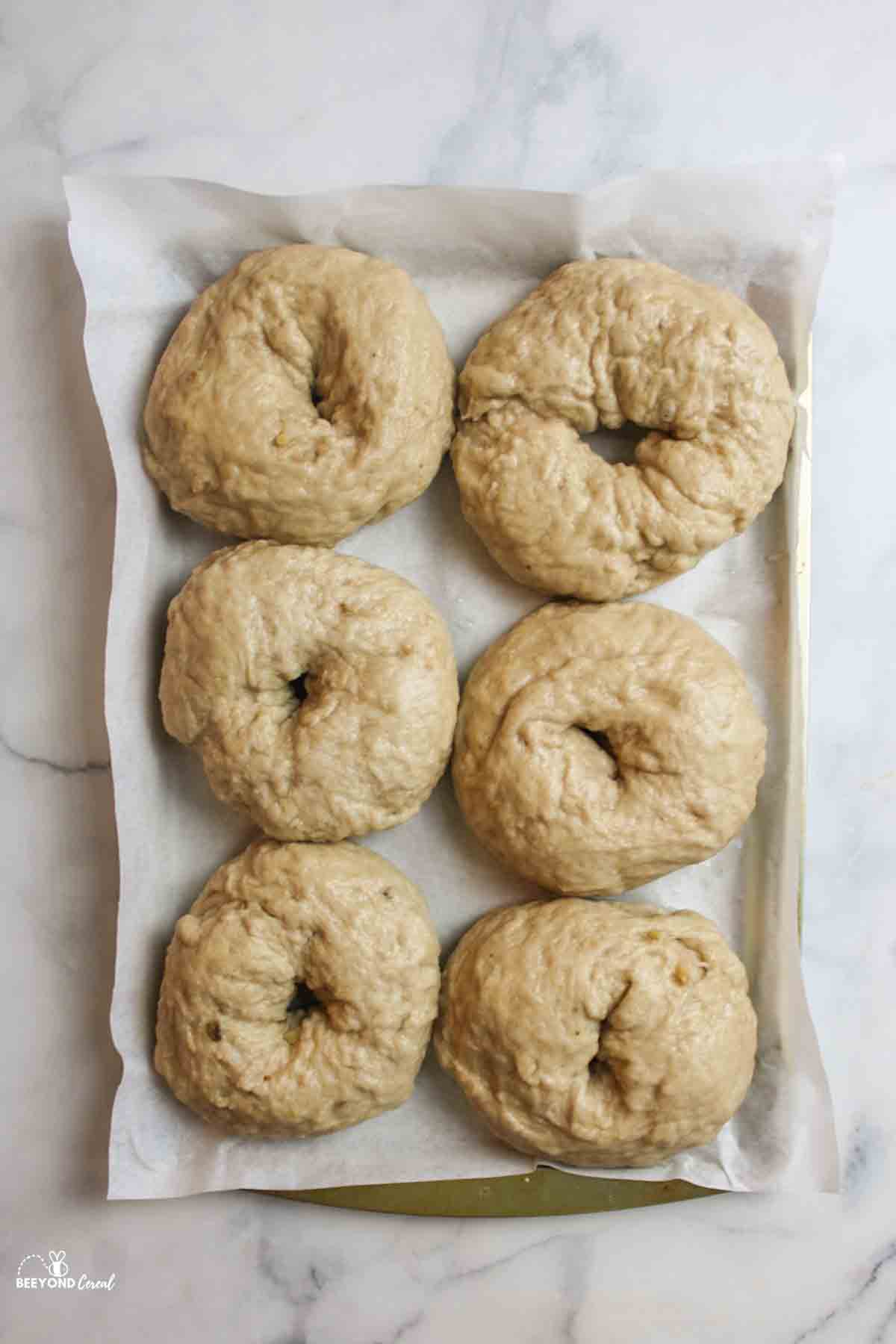 6 boiled banana bagels on a parchment paper lined baking sheet.