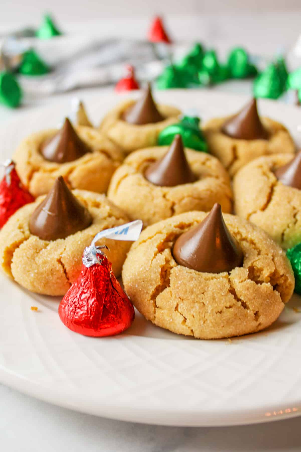 Peanut butter blossom cookies on white plate with wrapped seasonal Hershey Kisses.