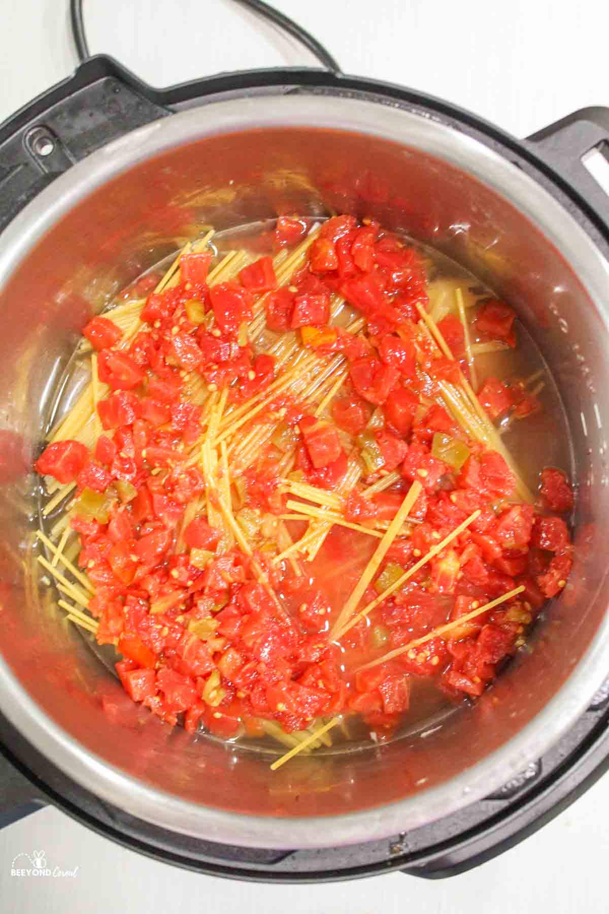 tomatoes topped over spaghetti noodles and liquid in instant pot