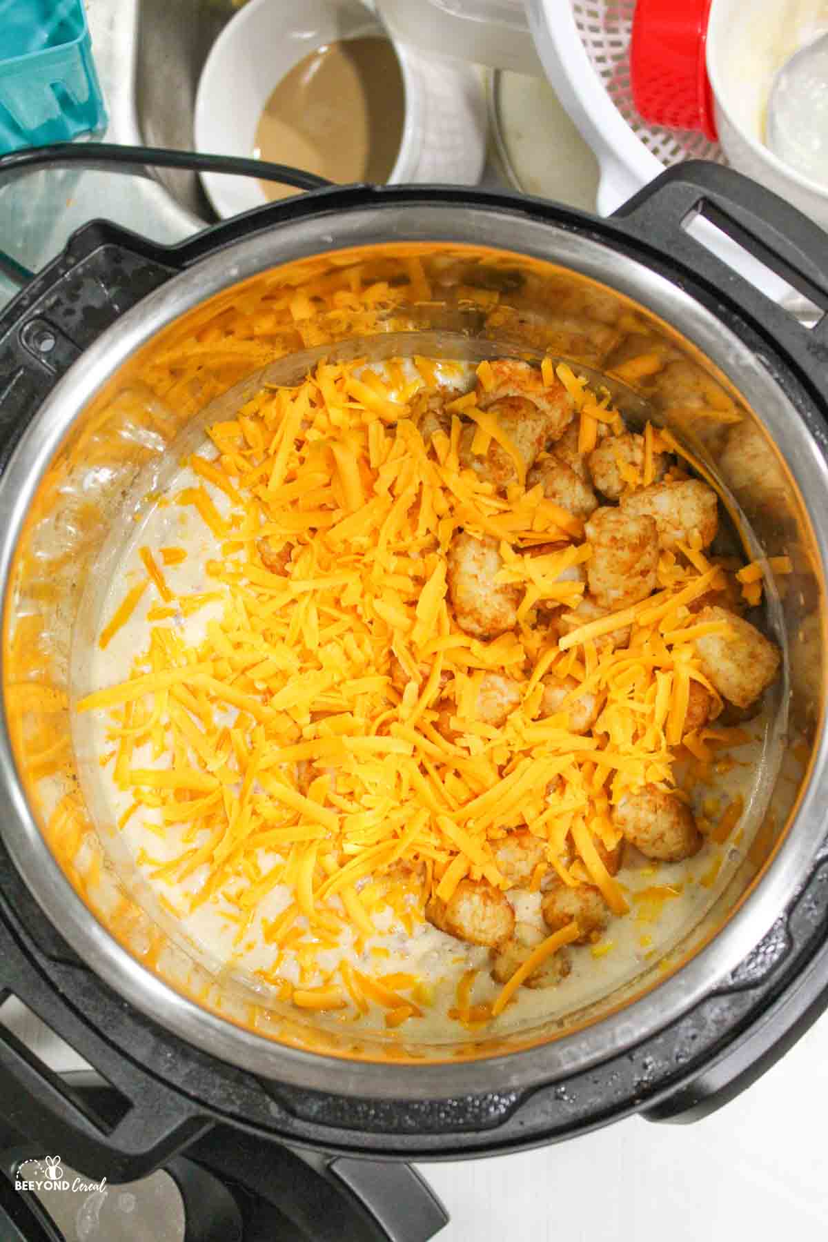 tater tots added to instant pot with creamy misture and shredded cheese.