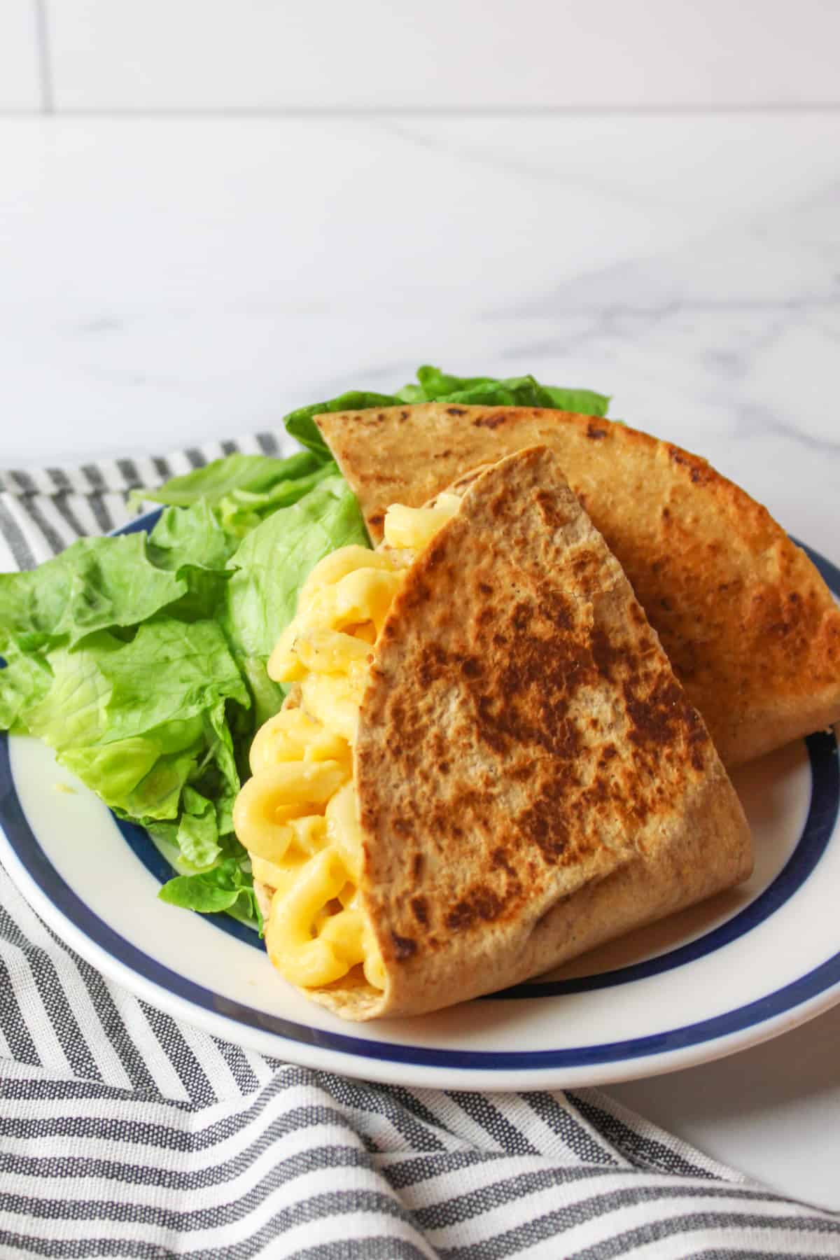 two halves of mac and cheese stuffed quesadilla on a plate with green salad