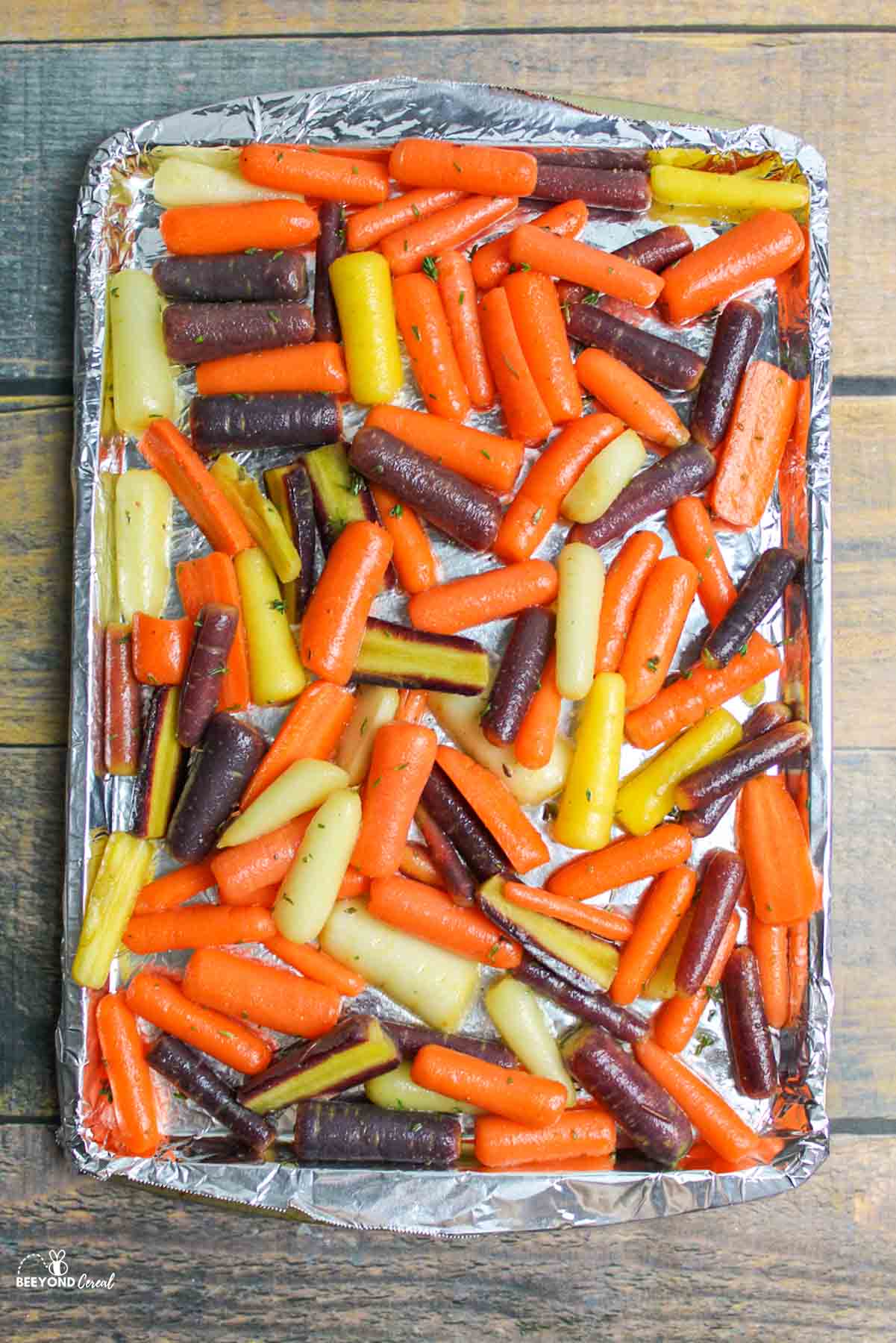 baby carrots spread out on a foil lined baking sheet