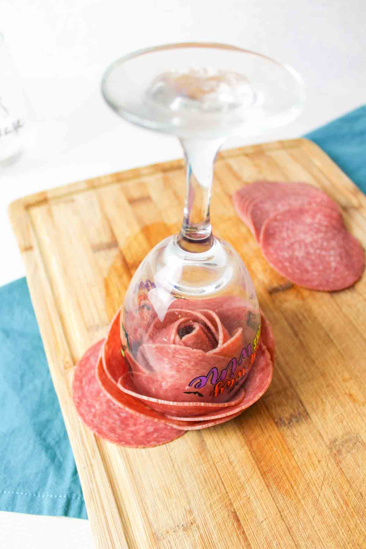 wine glass with folded deli meat over the rim turned upside down to show a rose inside.