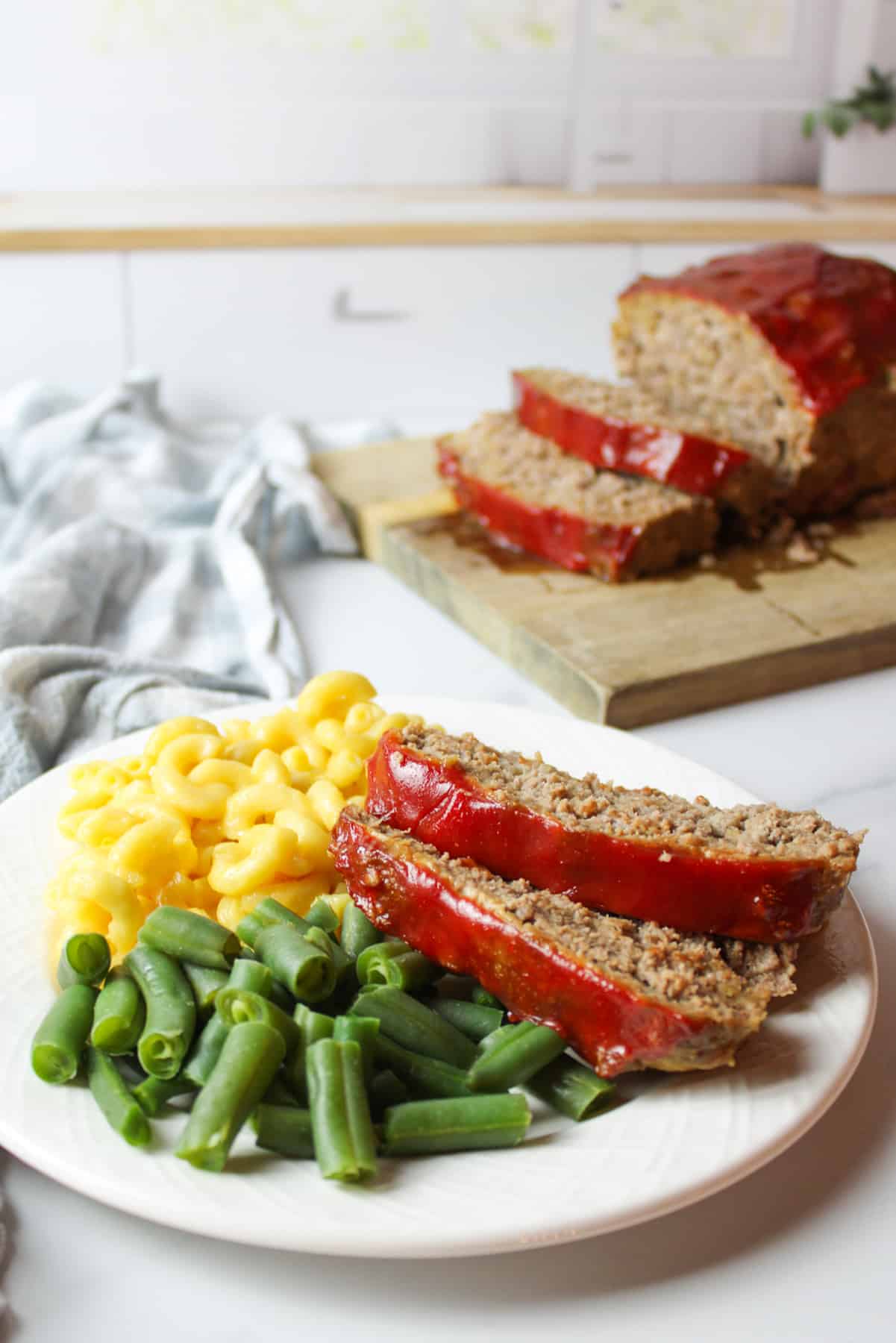 meatloaf sliced and served on a dinner plate with macaroni and green beans.