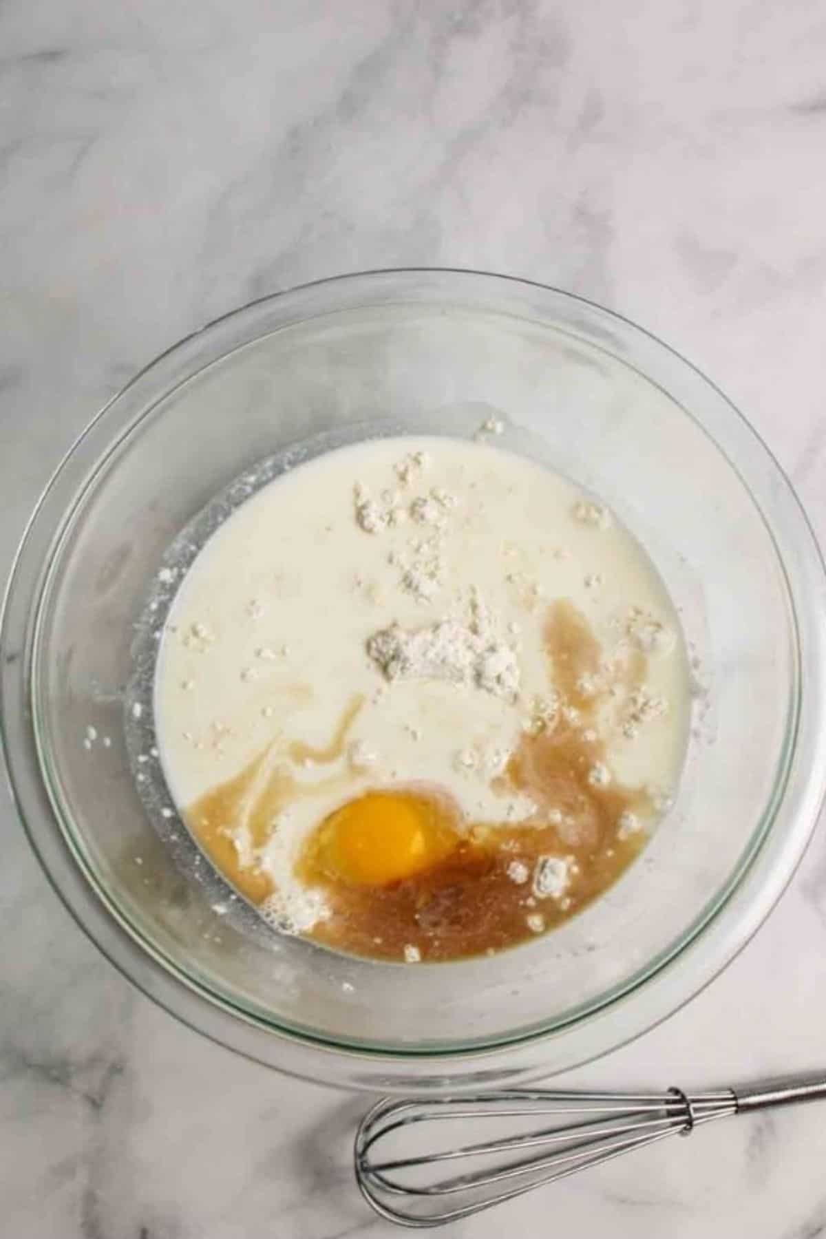 ingredients for crepes in a mixing bowl with a whisk to the side.