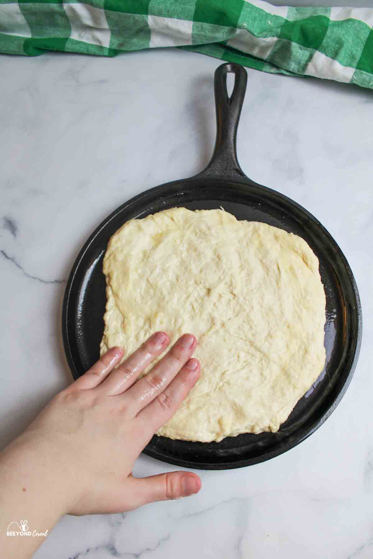 hand pressing dough out into a round circle on a greased iron skillet.