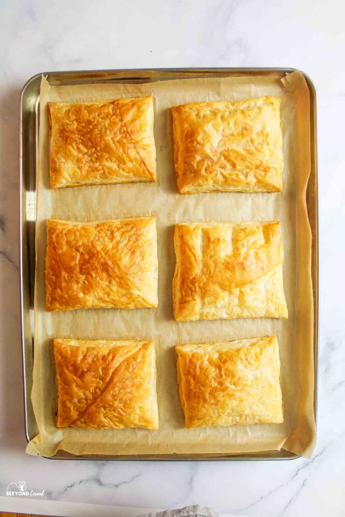6 baked squares of puff pastry on a parchment paper lined baking sheet