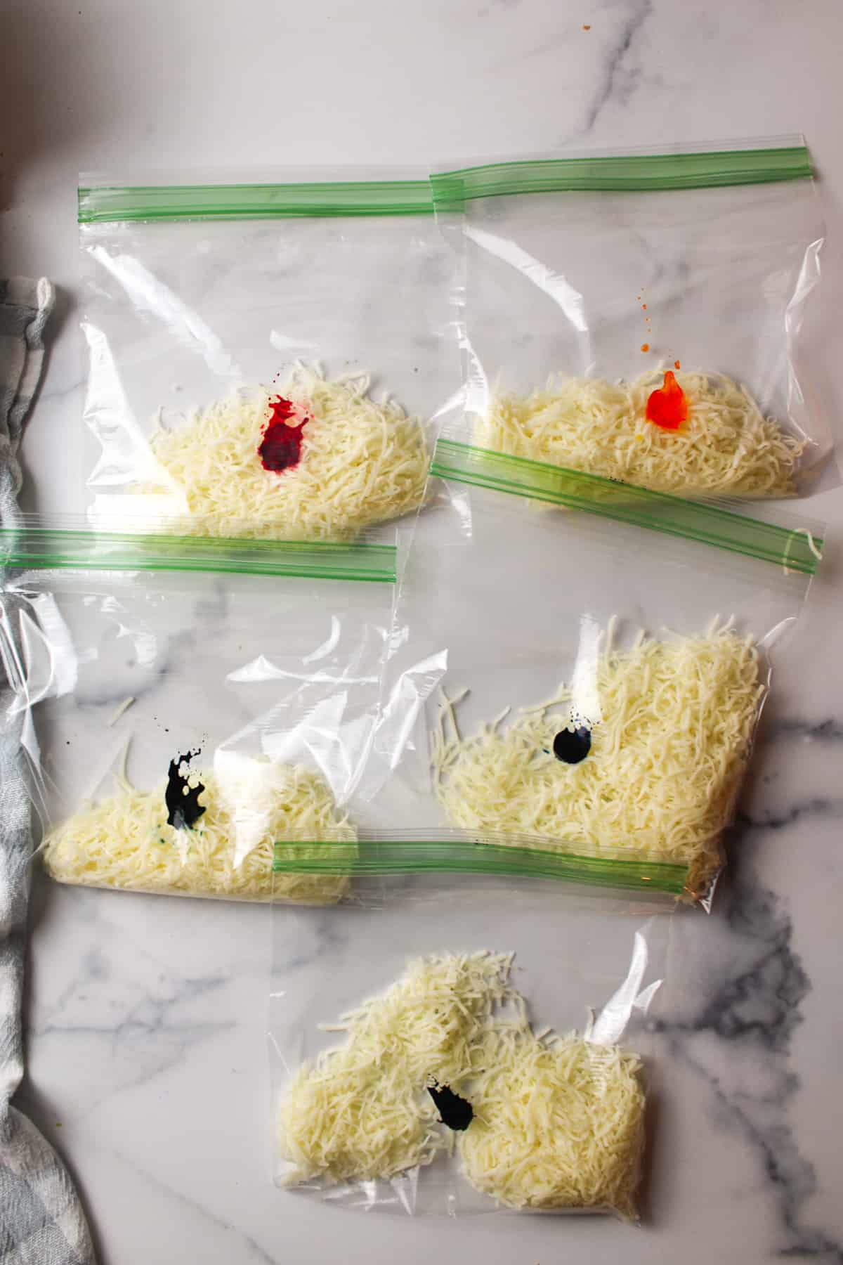 divided white shredded cheese in bags with dots of food coloring in each