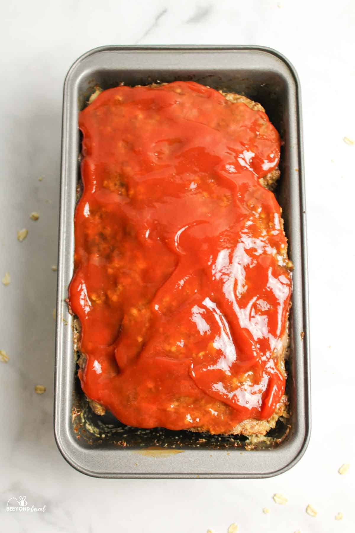 ketchup spread over the top of oatmeal meatloaf in a bread loaf pan