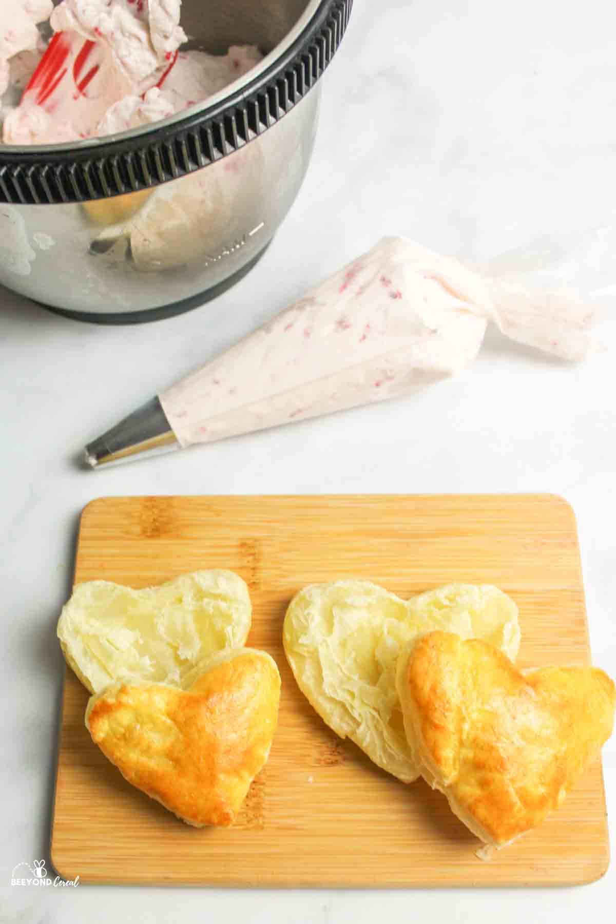 two halved puff pastry hearts on a cutting board with whipped cream in background