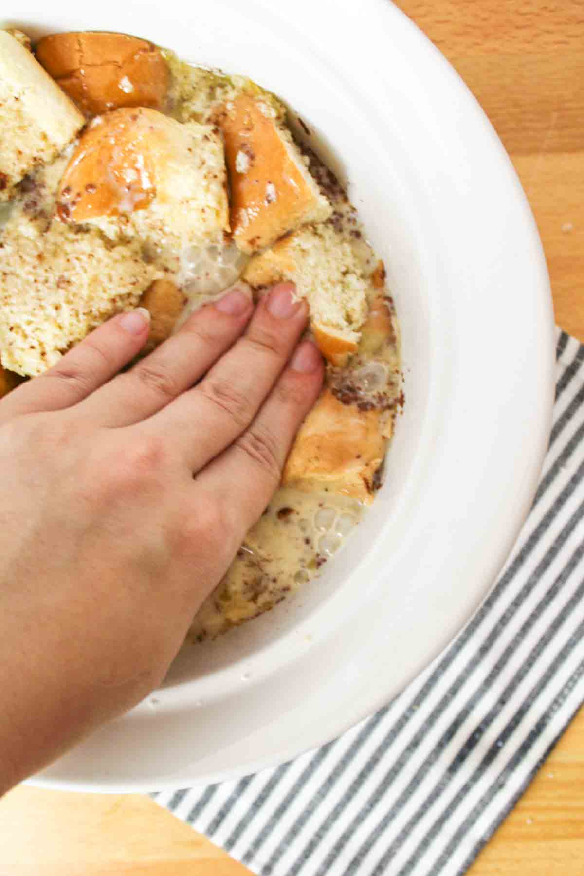 hand pressing down on the cubed bread so that it soaks in more moisture.