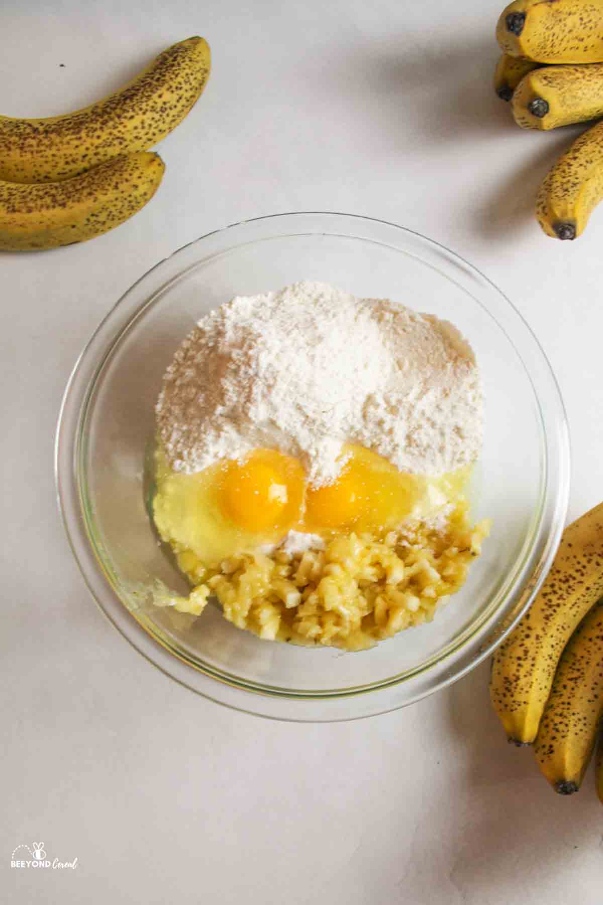 cake mix eggs and mashed banana in a mixing bowl with ripe bananas around it.