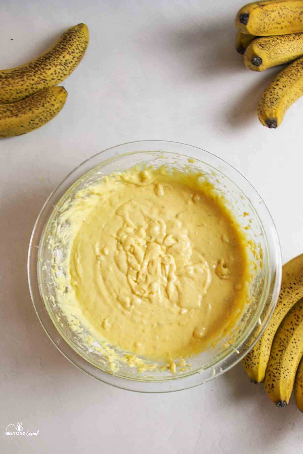 banana bread batter in a mixing bowl with ripe bananas to the sides.