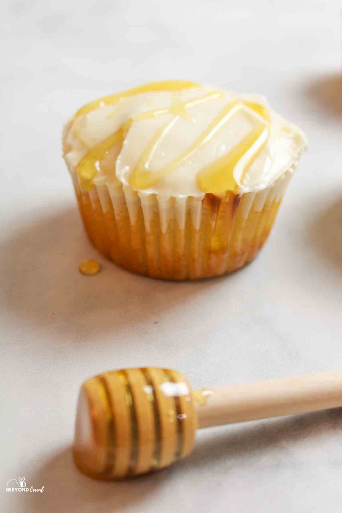 honey drizzled over frosted honey bee cupcake with honey stick to the front.