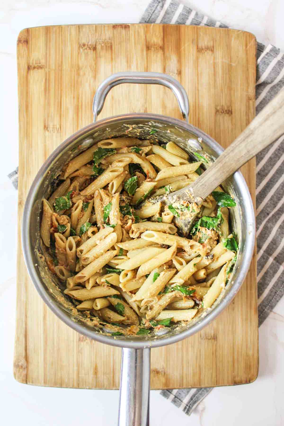 Wooden spoon stirring cream cheese mixture, spinach into cooked pasta.