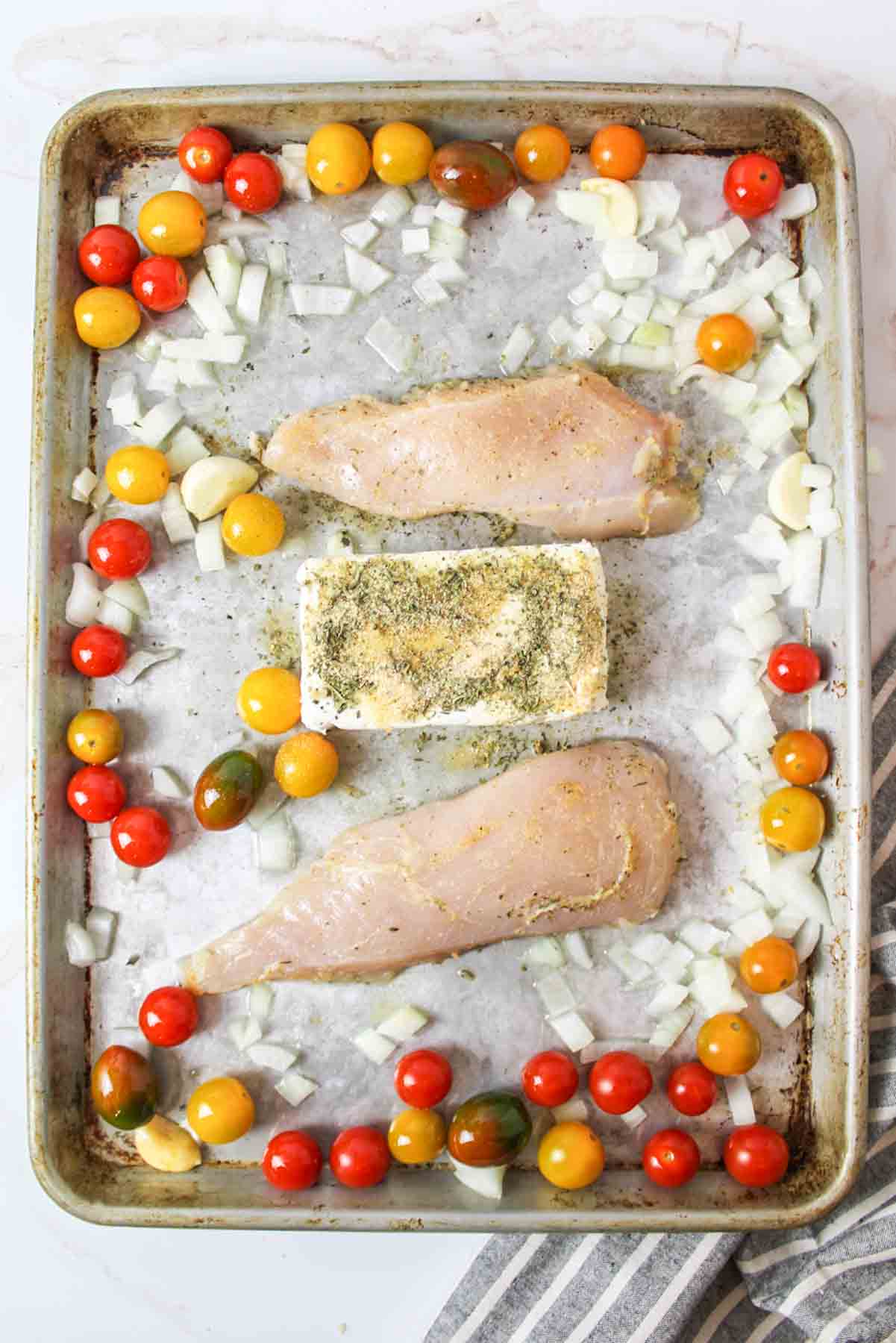 Seasoned chicken breasts, cream cheese, garlic, tomatoes, onions on sheet.