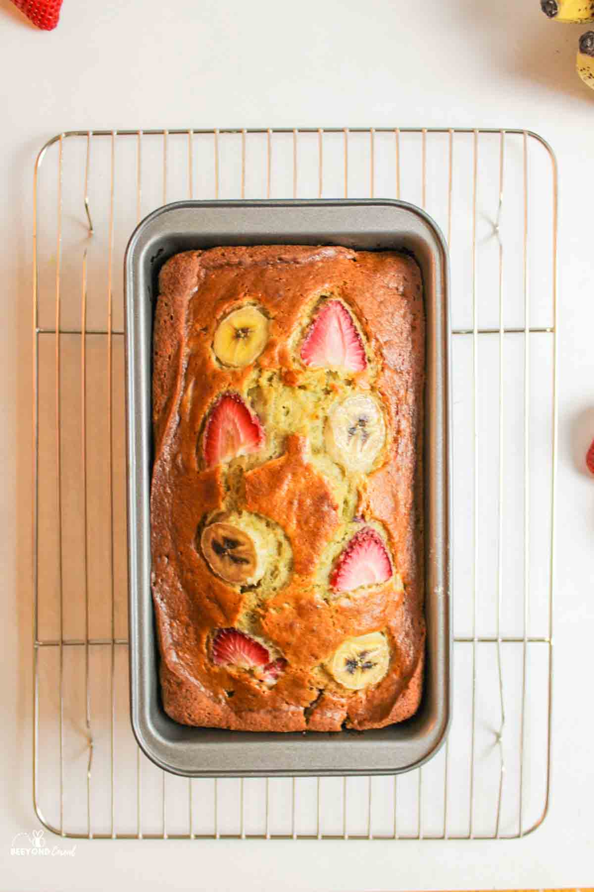 aerial view of strawberry banana bread in a bread pan on a cooling rack