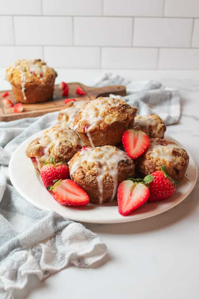 a white plate topped with icing covered bakery style strawberry muffins.