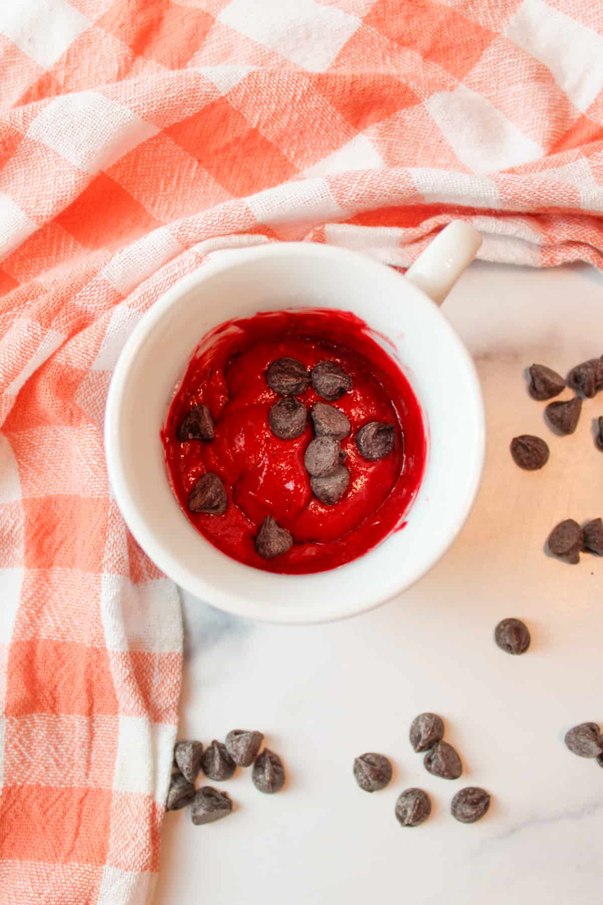 red velvet cake batter in a mug with chocolate chips inside and around the mug