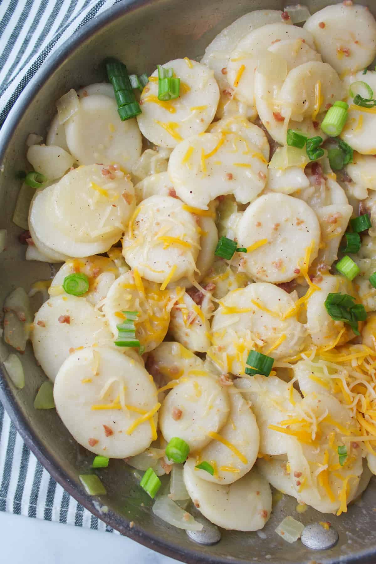 breakfast potatoes in a skillet topped with cheese and green onions.