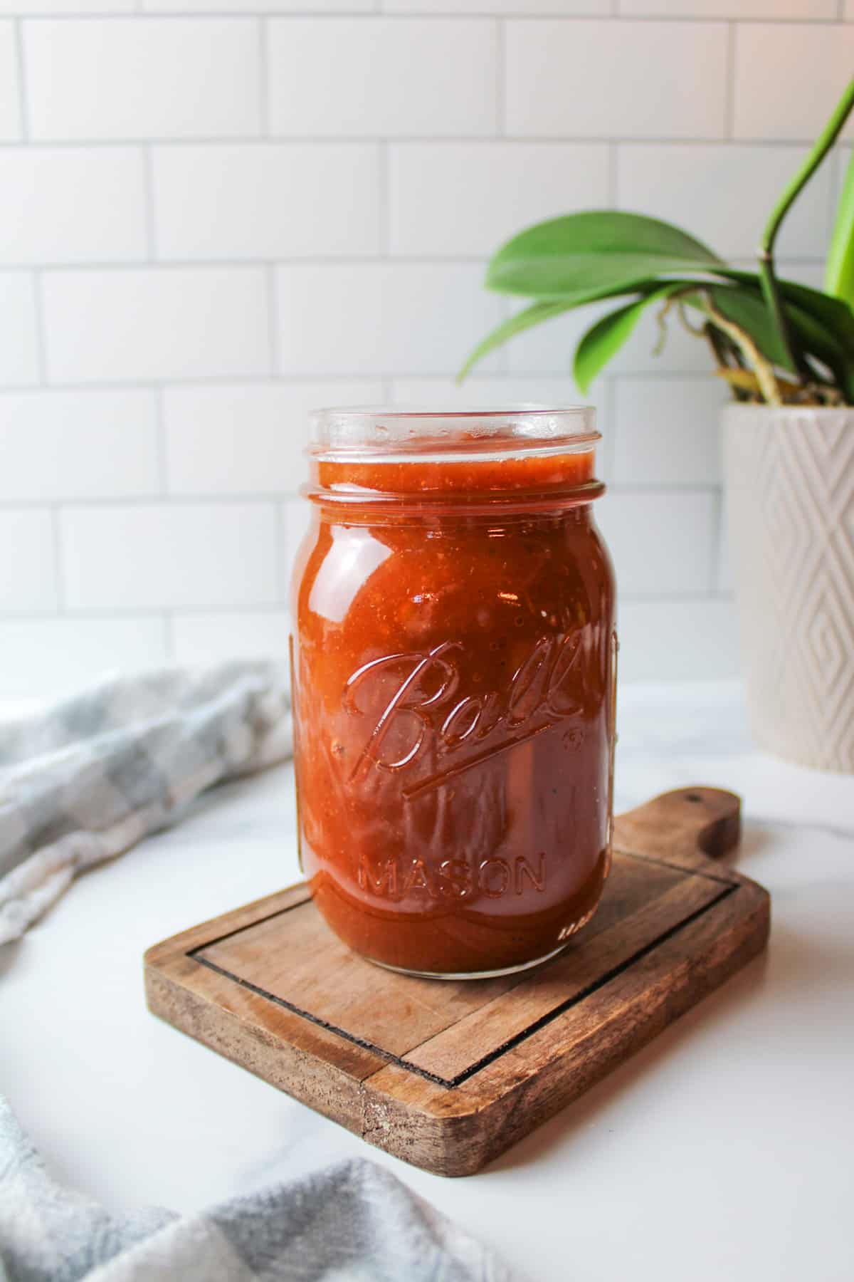 a ball mason jar filled with homemade bbq sauce with a green leaf plant in the background.