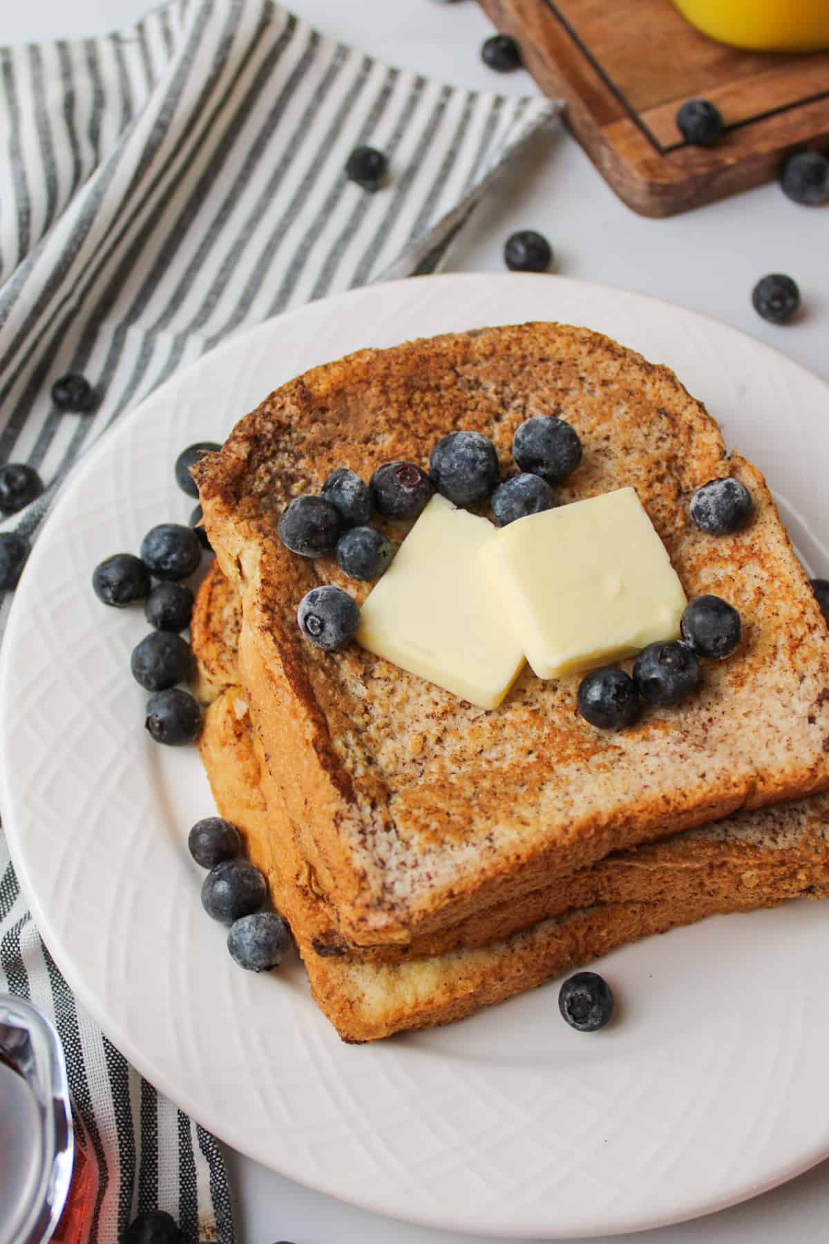 stacked french toast on a plate with blueberries and sliced butter.