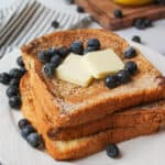 an upclose view of stacked french toast on a plate topped with butter slices and blueberries