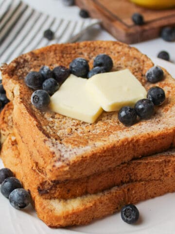 stacked french toast on a plate topped with butter slices and blueberries.