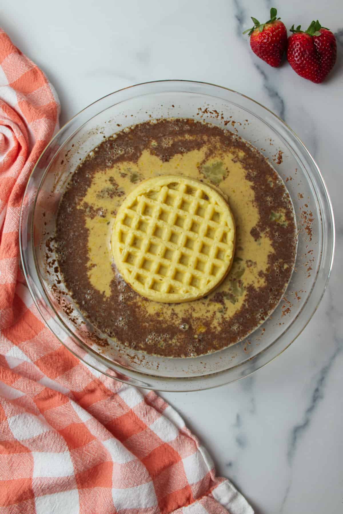 eggo waffle added to cinnamon spiced egg mixture in a pie plate